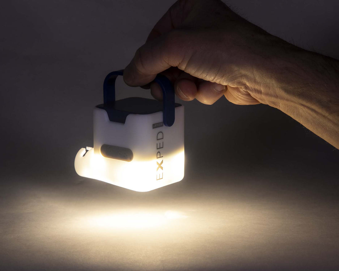 Hand holding an Exped device used as a lantern, illuminating a surface in the dark.
